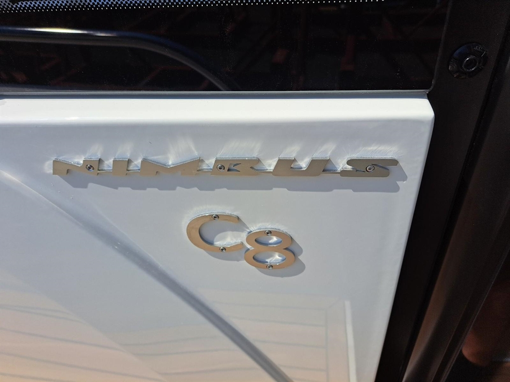 White door of a Nimbus C8 boat, featuring the metallic 'NIMBUS' logo and 'C8' model number, reflecting sunlight.
